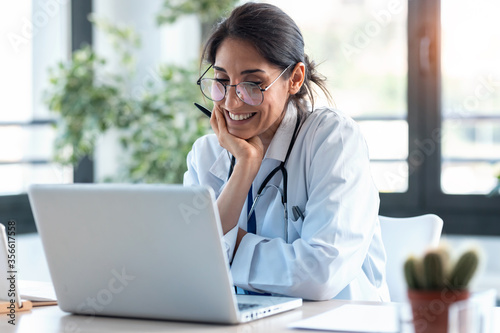 Smiling female doctor working with her laptop in the consultation.