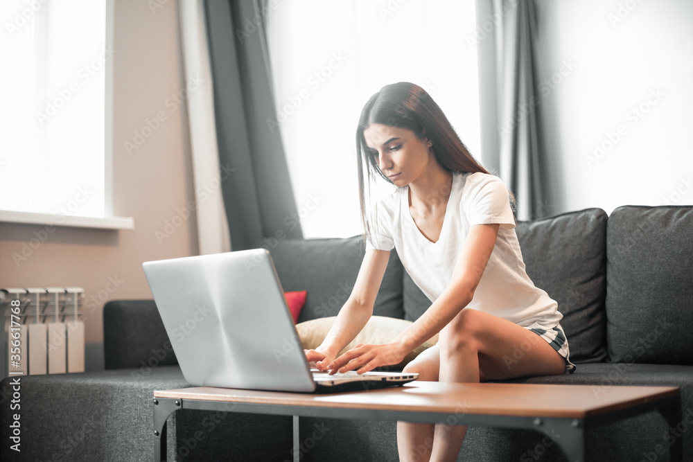 Young woman with modern laptop sitting on sofa at home Young woman with modern laptop sitting on sofa at home