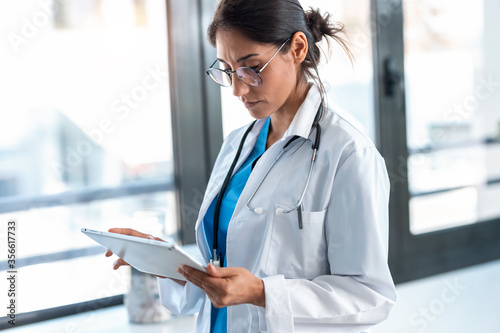 Beautiful female doctor using her digital tablet while standing in the consultation.