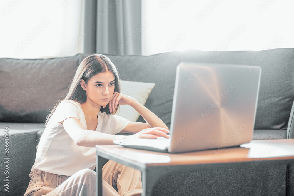 Fototapeta premium Young woman with modern laptop sitting on sofa at home