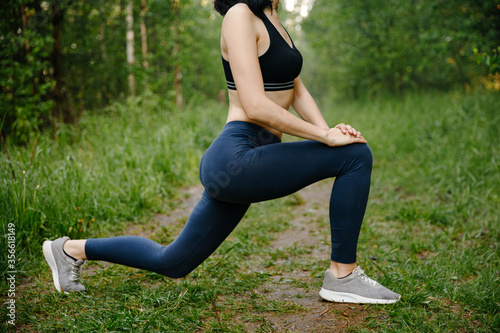 The girl is engaged in outdoor sports in the green forest, exercises with stretching her legs. Close up. The concept of a healthy lifestyle