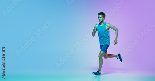 Portrait of young caucasian man running, jogging on gradient studio background in neon light. Professional sportsman training in action, motion. Sport, wellness, activity, concept. Flyer with © master1305