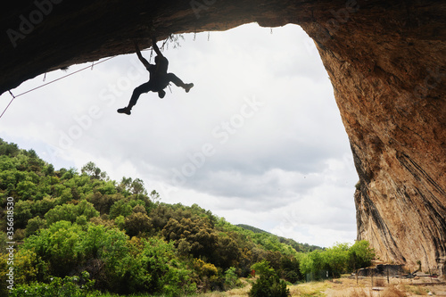 Young man climbing a collapsed wall inside a cave with his legs in the air. Cloudy sky background.