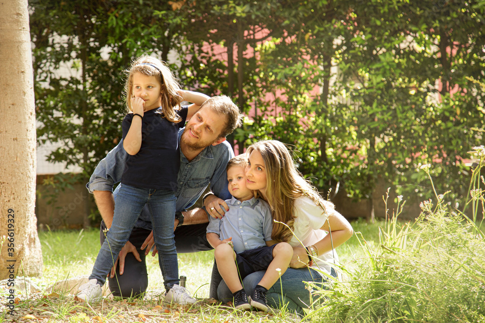 Fototapeta premium Bellissima famiglia composta da 2 genitori e figli si raduna felice in gruppo nel giardino di casa