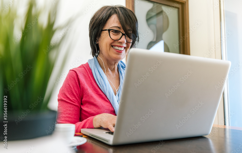 Senior older woman working with laptop computer on the table at home indoor. Old mature people and technology concept - obrazy, fototapety, plakaty 