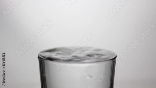 Drops of water falling into a glass full of water; pure and transparent water; drip, drop by drop