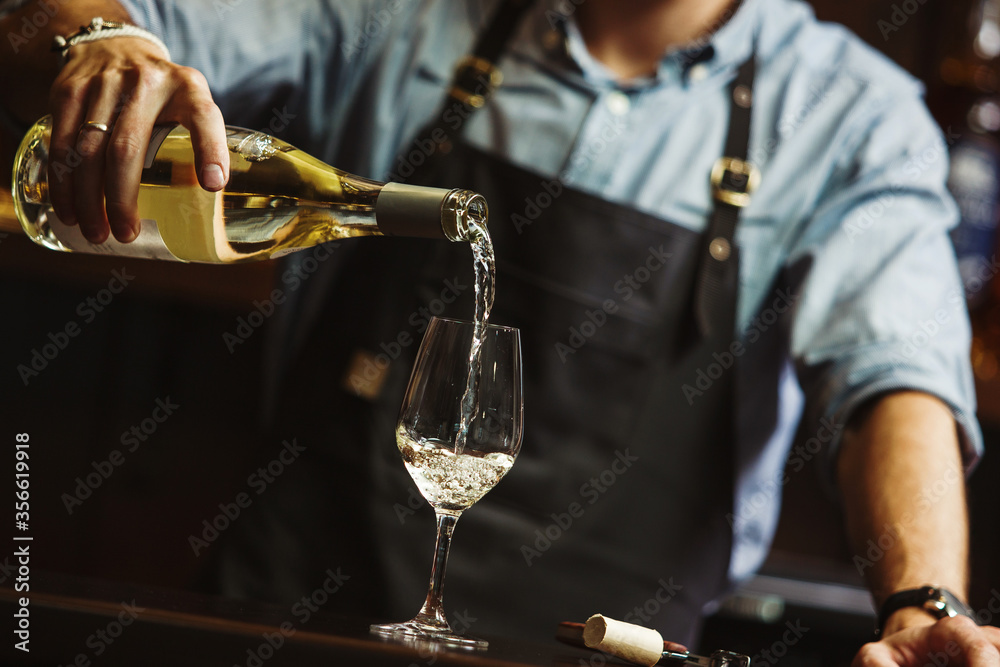 Male sommelier pouring white wine into long-stemmed wineglasses.