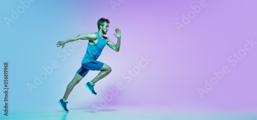 In jump. Portrait of young caucasian man running  jogging on gradient studio background in neon light. Professional sportsman training in action and motion. Sport  wellness  activity  concept. Flyer.