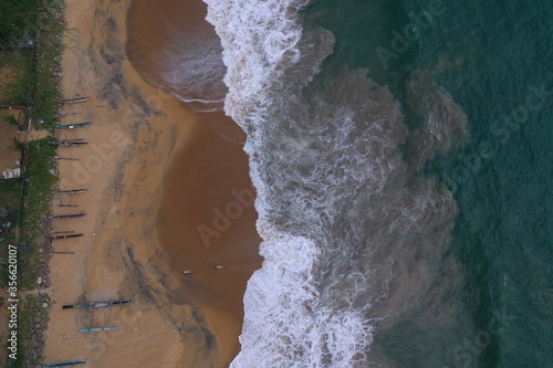 aerial drone bird view shot of the sea shore with turquoise water, an empty yellow sand beach with fishing long boats, white waves and foam forming beautiful textures, patterns, shapes. Sri Lanka