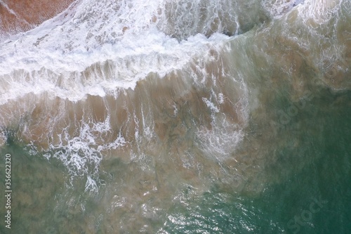 aerial drone bird view shot of the sea surface with turquoise blue water, large white waves, foam and underwater sand forming beautiful textures, patterns, shapes. Sri Lanka