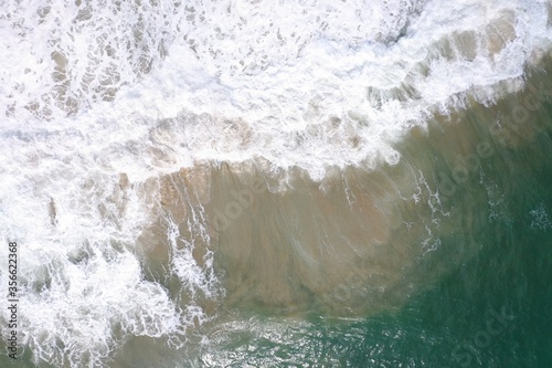 aerial drone bird view shot of the sea surface with turquoise blue water, large white waves, foam and underwater sand forming beautiful textures, patterns, shapes. Sri Lanka