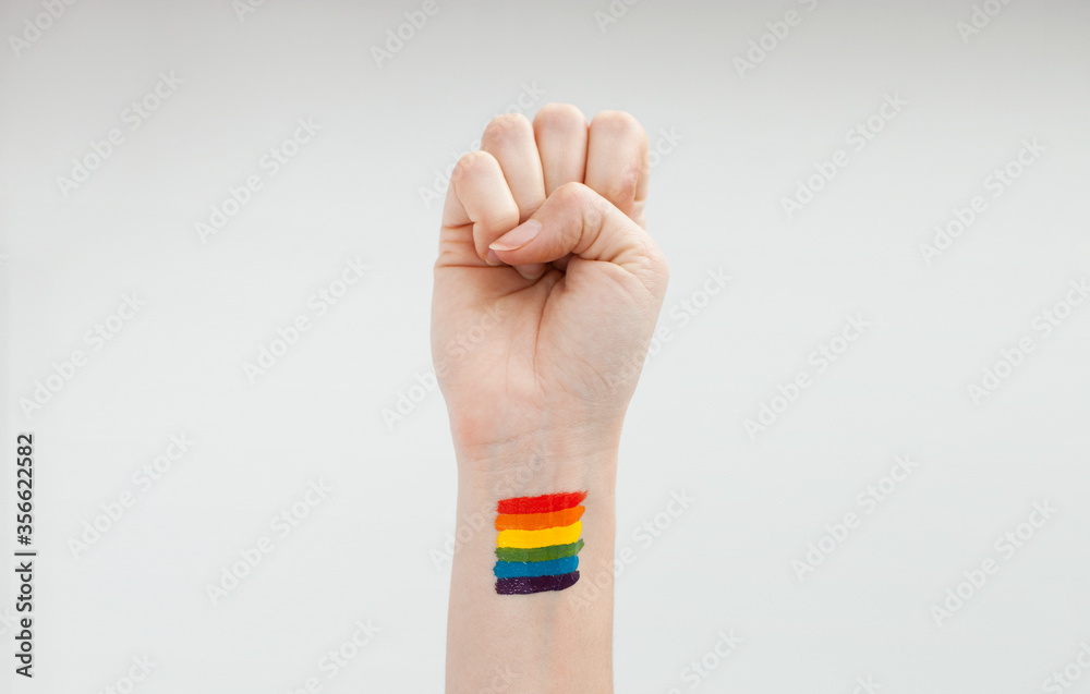A hand raised in support for lgbtq+ community with a rainbow painted on the wrist in honour of pride month A hand raised in support for lgbtq+ community with a rainbow painted on the wrist in honour of pride month
