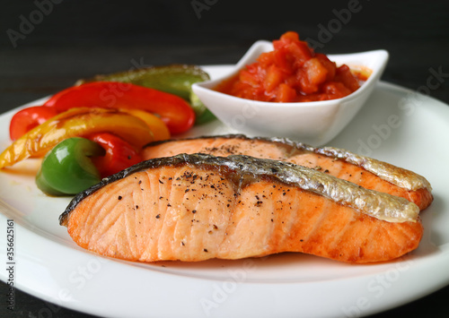 Homemade pan seared salmon steaks with grilled colorful vegetables and salsa on white plate