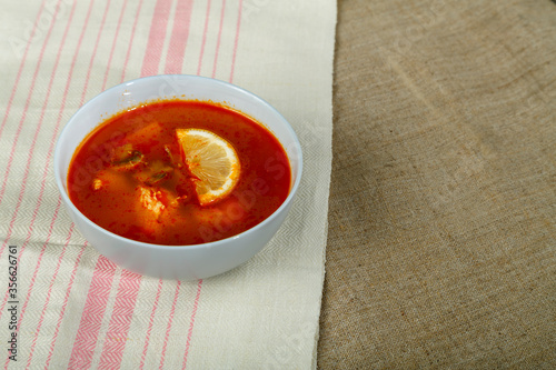 Traditional Tom Yum soup with chicken in a plate on a tablecloth on a linen napkin.