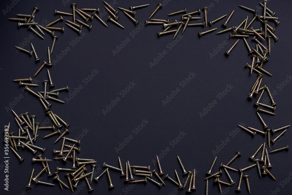 Light wood screws lie like a frame on a black background, in the middle there is an empty space - workspace, place for text