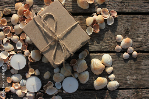 Brown gift box, tea candles, and seashells on the natural weathered old wooden background with copy space. Top view. Summer birthday present 