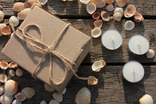 Brown gift box, tea candles, and seashells on the natural weathered old wooden background with copy space. Top view. Summer birthday present
