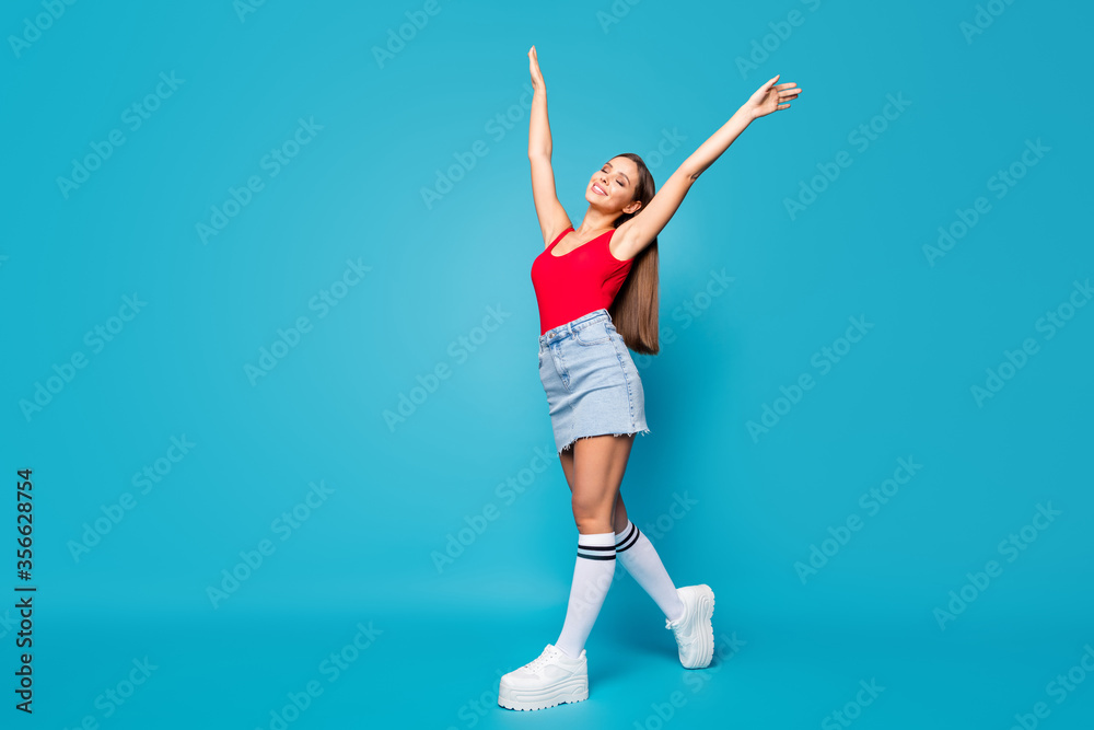 Full body profile side photo of calm cheerful satisfied youth lady go walk enjoy spring wind air raise hands arms wear tank-top gumshoes isolated over blue color background Full body profile side photo of calm cheerful satisfied youth lady go walk enjoy spring wind air raise hands arms wear tank-top gumshoes isolated over blue color background