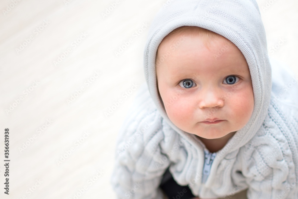 close up portrait of baby sitting on light floor and looking up, face of cute baby with blue eyes lookin at camera, baby with hood, view from above close up portrait of baby sitting on light floor and looking up, face of cute baby with blue eyes lookin at camera, baby with hood, view from above