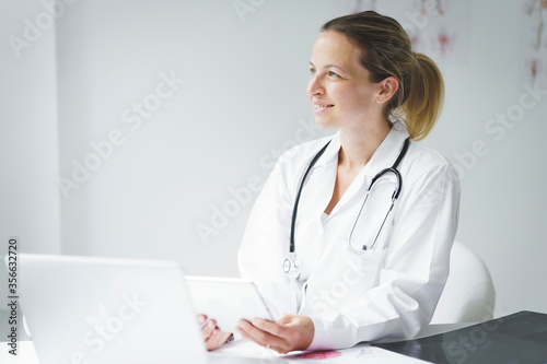 young, attractive blonde doctor is sitting in her office, working on her tablet and looking at examination results