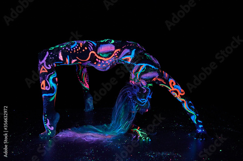 Art woman body art on the body dancing in ultraviolet light. Bright abstract drawings on the girl body neon color. Fashion and art woman, out of focus © angel_nt