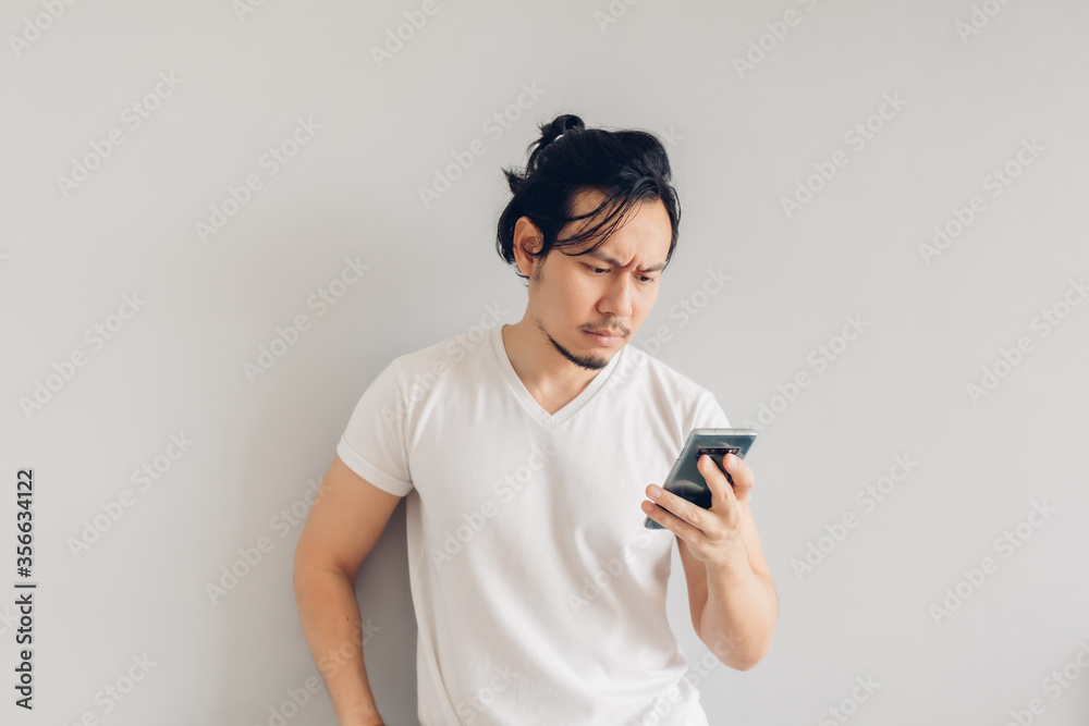Serious long hair Asian man in white casual t-shirt is using smartphone. Serious long hair Asian man in white casual t-shirt is using smartphone.