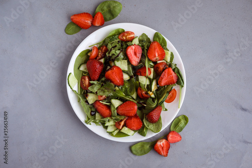 Tasty summer salad made of strawberries, arugula, spinach, little tomatoes, cucumbers and balsamic sauce. Top view.