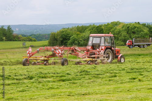 A tractor with a rotary rake rakes freshly cut grass for silage in the field. photo