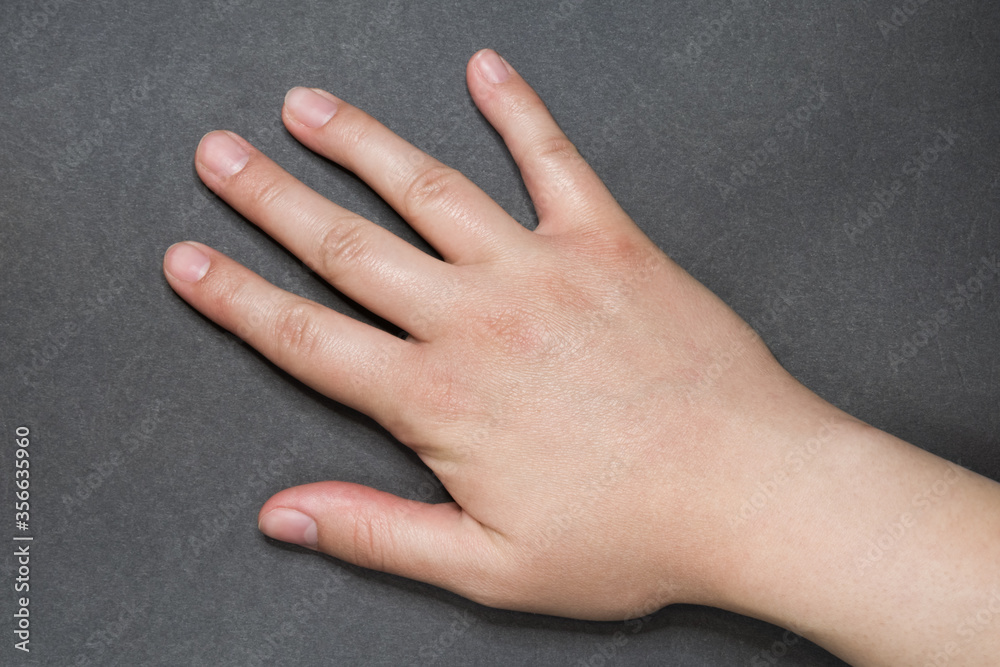 Young white female right hand with natural manicure on grey surface Young white female right hand with natural manicure on grey surface