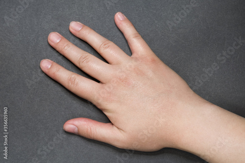 Young white female right hand with natural manicure on grey surface