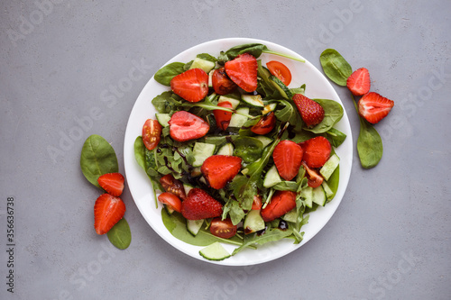 Tasty summer salad made of strawberries, arugula, spinach, little tomatoes, cucumbers and balsamic sauce. Top view, flat lay.