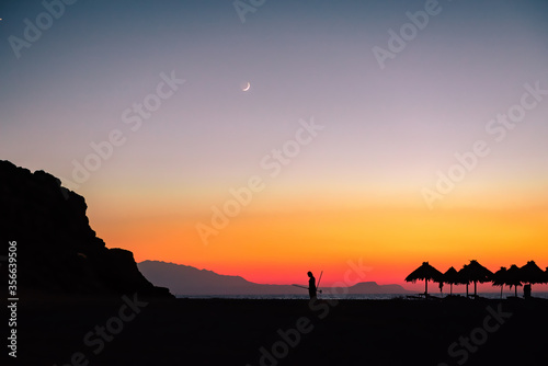 Silhouette image of summer sunset at the beach. Crescent moon in the sky