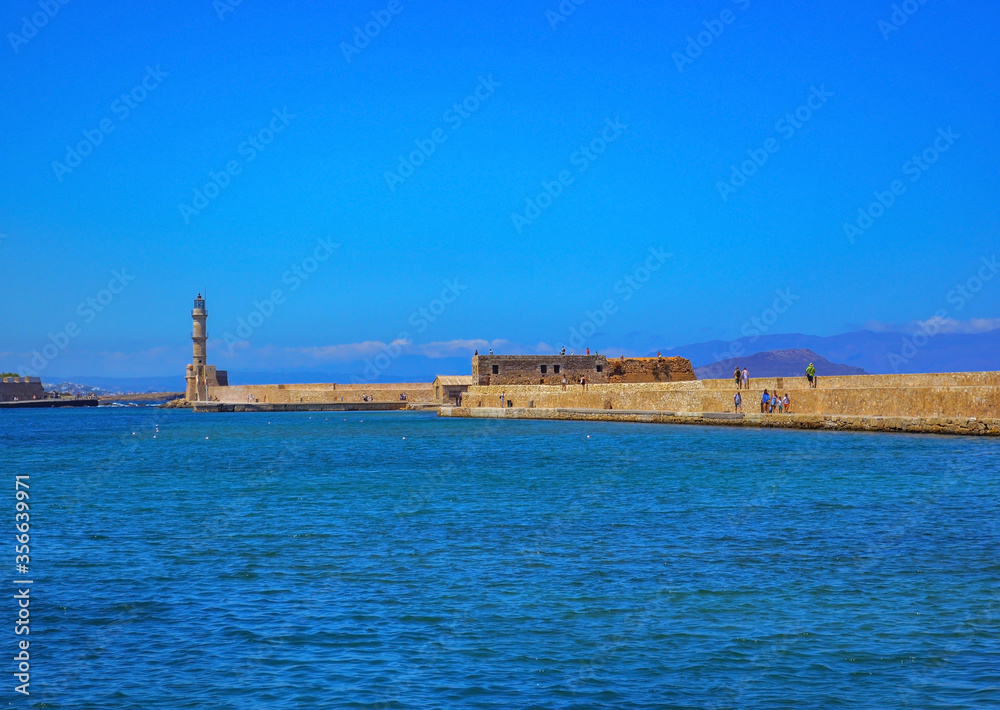 People are walking over remains of old Venetian fortification with lighthouse in Chania, Crete, Greece.