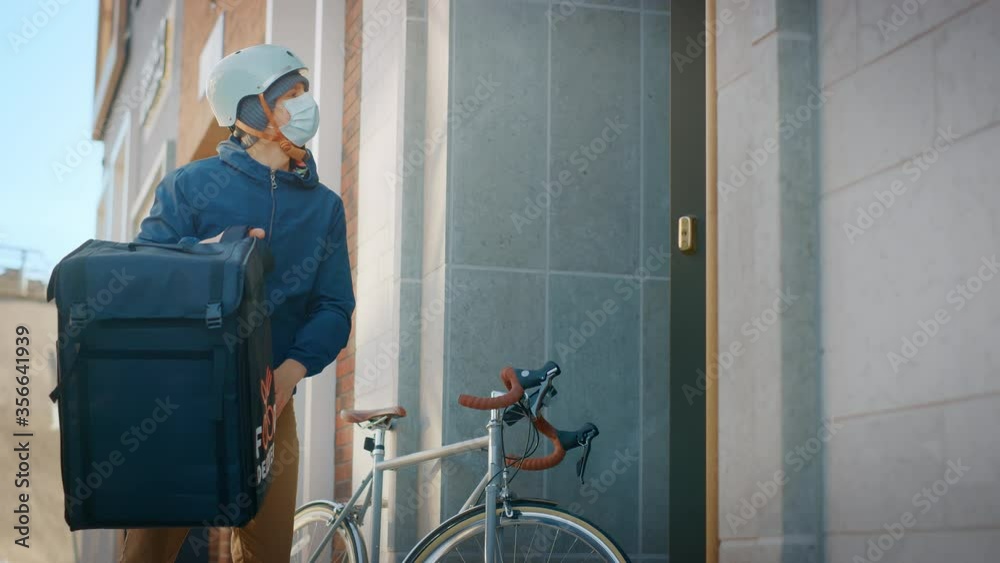 Food Delivery Man Wearing Protective Medical Face Mask and Thermal Backpack Rides a Bike to Deliver Order to a Masked Female Customer. Courier Delivers Takeaway Lunch. Quarantine, Social Distancing Food Delivery Man Wearing Protective Medical Face Mask and Thermal Backpack Rides a Bike to Deliver Order to a Masked Female Customer. Courier Delivers Takeaway Lunch. Quarantine, Social Distancing