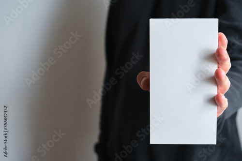 Man holding in hand small paper box. Blank packing, empty space. Male with a new package. Postal service, delivery. White paper. Gift box, present. Box close up. People communication. Carton case