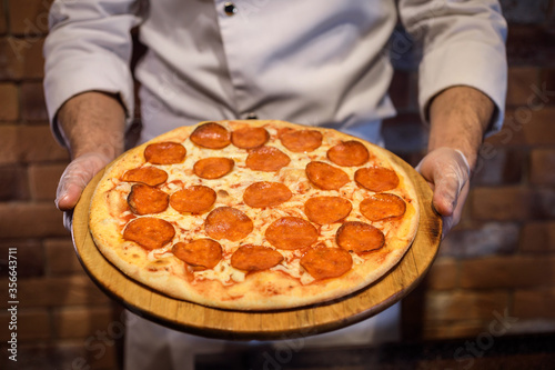 Pepperoni pizza in the chef's hands. Appetizing meal from the Italian cuisine. Restaurant menu presentation.