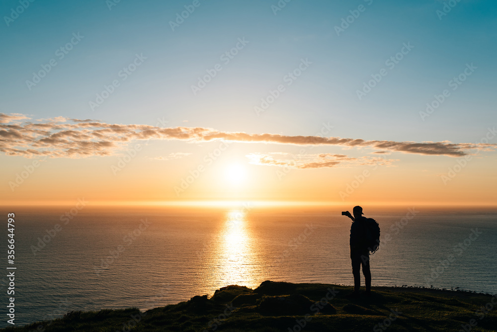 Silhouette of a young hiker taking pictures of sunset
