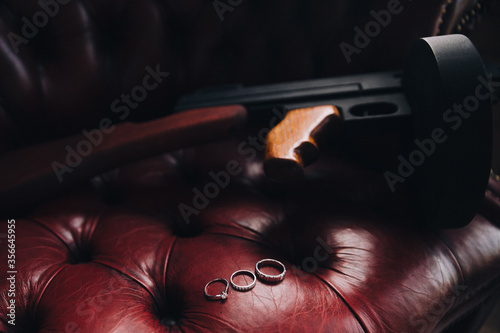 Wedding rings lie on a leather chair next to a mock Thompson machine gun photo