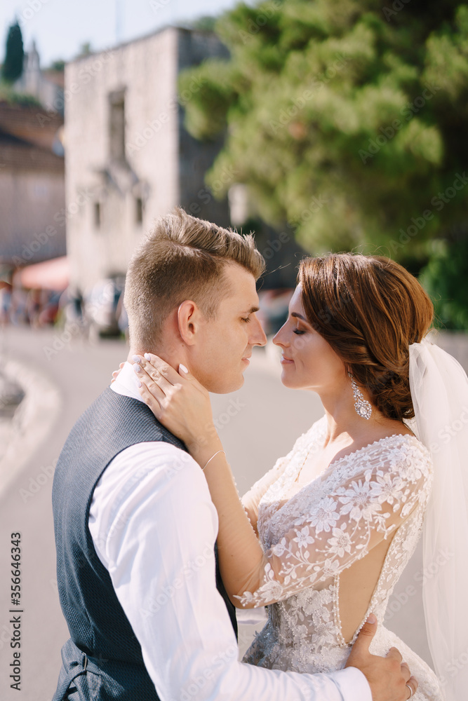 Portrait of a wedding couple on the street, the bride hugs the groom by the neck, the groom hugs her around the waist. Fine-art wedding photo in Montenegro, Perast. 