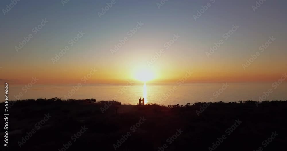 Couple in love, standing on a cliff, looking out at the horizon, watching the sunrise. Aerial Drone fly over Point Dume in Malibu, California. Couple in love, standing on a cliff, looking out at the horizon, watching the sunrise. Aerial Drone fly over Point Dume in Malibu, California.