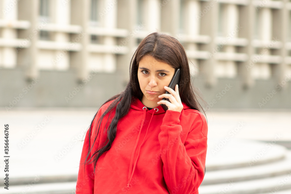 The girl looks in camera with an offended look, speaks on a smartphone on the street The girl looks in camera with an offended look, speaks on a smartphone on the street