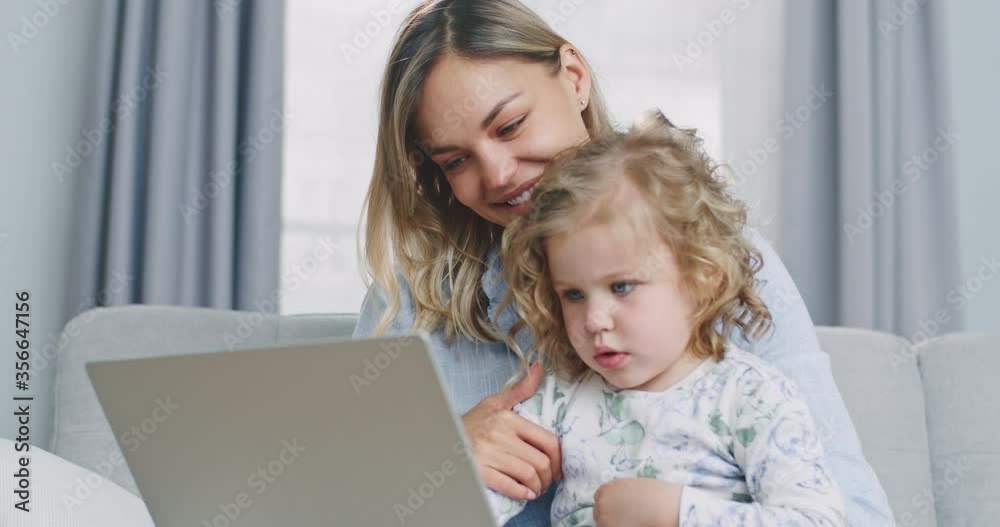 Middle plan of happy family young mother and child daughter looking at camera webcam talking making online video call having conversation laughing embracing communicating online. Middle plan of happy family young mother and child daughter looking at camera webcam talking making online video call having conversation laughing embracing communicating online.