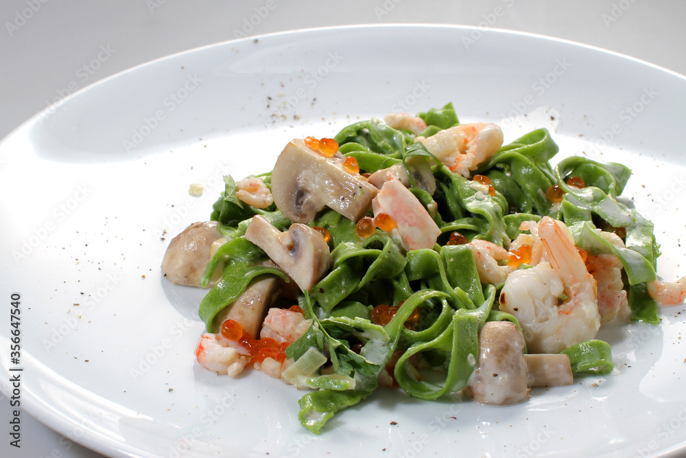 Green noodles with spinach, shrimp, caviar and mushrooms on a white plate Green noodles with spinach, shrimp, caviar and mushrooms on a white plate
