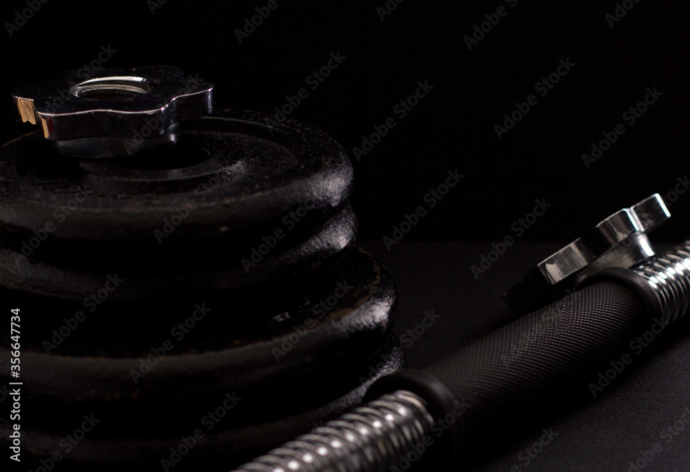 Black metal dumbbell for fitness with a chrome handle, on a black background. Black metal dumbbell for fitness with a chrome handle, on a black background.
