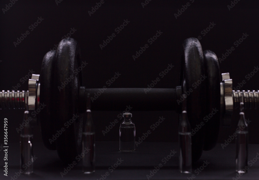 Black metal dumbbell for fitness with ampoules, on a black background.