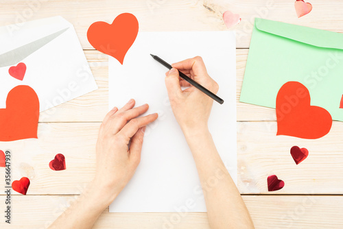 Girl's hand writes a love letter. Valentine's Day. Handmade greeting card with a red heart in the shape of a figure. February 14th is a celebration of celebration. View from above