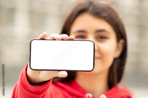 Front view of happy woman showing smartphone with blank screen in the street
