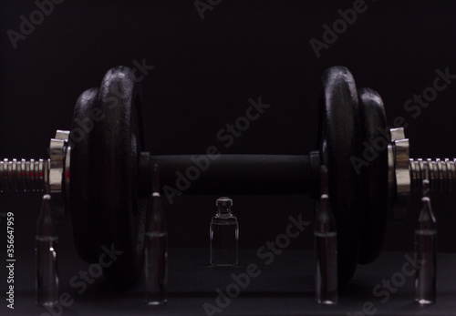 Black metal dumbbell for fitness with ampoules, on a black background.