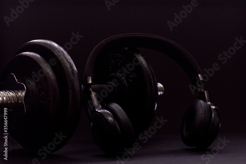 Black metal dumbbell for fitness with headphones, on a black background.