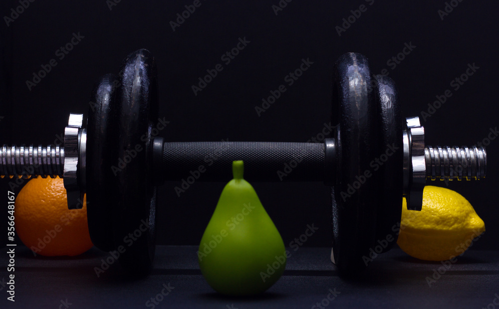 Naklejka premium Black metal dumbbell for fitness with fruits, on a black background.